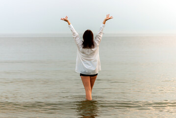 Young woman enjoying freedom with open hands on a sea.Attractive,young woman with hands up.Summer vacation.Rear view.