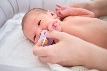Newborn baby with a pacifier in the mouth and mother hand. Child boy in a cocoon on a crib with mom