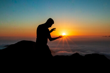 Silhouette of a man touching the sun with both hands on top of a mountain. sunset and cloud sky background.
