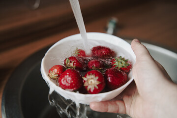 Washing up ripe strawberries in glass bowl. Rinsing red summer berries full of vitamins.