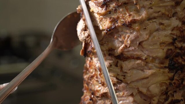 the chef cuts the shawarma on a spit with a large knife