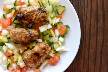 Sheftalia : Cypriot Lamb and Pork Sausages. Grilled Sausages with Fresh Vegetables (Cucumber, Tomato Onion) on a White Plate. Traditional Cypriot food. - obrazy, fototapety, plakaty