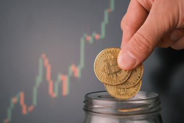 Man tosses a few bitcoin into a glass jar or piggy bank to accumulate a budget.