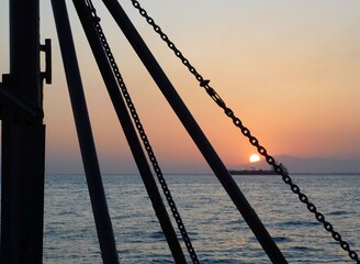 Sunset and a ship through the chains and rods of a winch