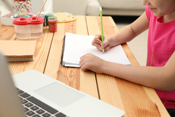 Little girl drawing on paper with pencil at online lesson indoors, closeup. Distance learning