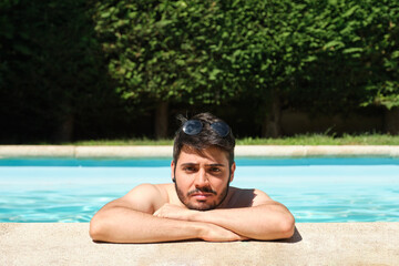 Portrait of a young man with sunglasses on his head, in a swimming pool looking at camera. Summer concept.