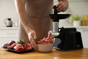 Man using modern meat grinder in kitchen, closeup