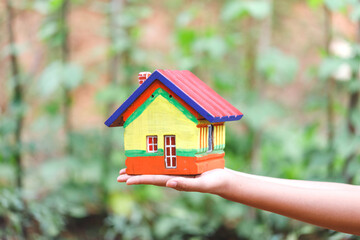 Wooden house model on woman hand green background.Property investment and house mortgage financial concept,