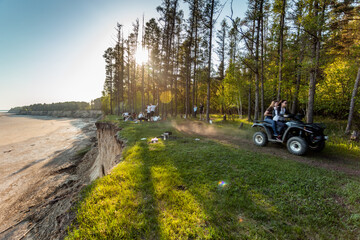 People have fun on the coast in the shade of the forest.  Guys ride ATVs. © Екатерина Акулова