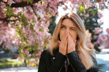 Woman suffering from seasonal pollen allergy near blossoming tree outdoors - obrazy, fototapety, plakaty