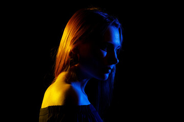 Portrait of a young woman in a colored side light on a dark background.