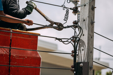 The electrician is using a wire cutter at a lamp post to install a street spotlight Led, workers, working about electrical outdoors at the height is risky.