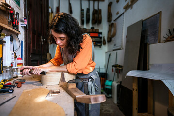 Obraz na płótnie Canvas woman luthier making guitars in her musical instrument workshop