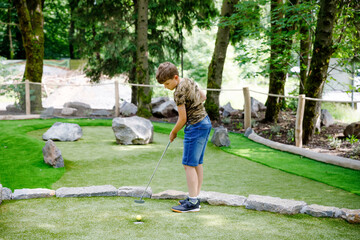 School kid boy playing mini golf with family. Happy child having fun with outdoor activity. Summer sport for children and adults, outdoors. Family vacations or resort. - obrazy, fototapety, plakaty