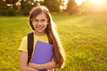 Happy schoolgirl in glasses standing in green park