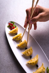 detail of the hand with chopsticks taking a Japanese ravioli from the plate