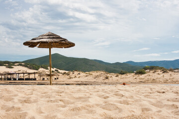 Fototapeta premium beach with wicker umbrella and mountains on background