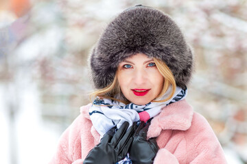 happy woman in a pink faux fur coat in winter on a background of snowy trees