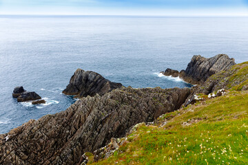 Rugged landscape at Malin Head, County Donegal, Ireland. Rough beach with cliffs, green rocky land with sheep on foggy cloudy day.