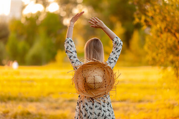 blonde with a straw hat rejoices in summer, view from the back