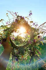 floral wreath in hand, sunny natural background. Summer Solstice Day, Midsummer concept. floral traditional decor. pagan witch traditions, wiccan symbol and rituals - obrazy, fototapety, plakaty