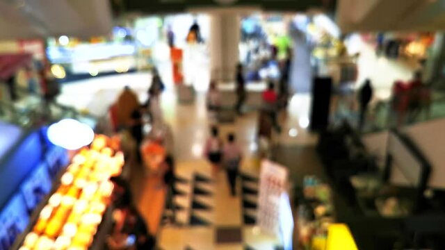 People are shopping for food, clothing and other items. in the department store On both sides are escalators, blurry images.