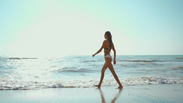slow motion footage of happy joyful fitness girl in bikini walks along sea beach with waves