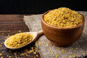 Bulgur in wooden bowl on dark wooden background.