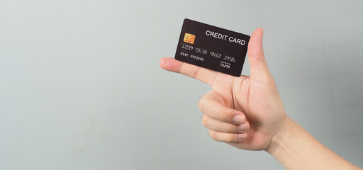 Hand is holding black credit card isolated on grey background.