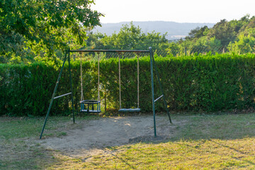 Image of some metal swings in a park surrounded by vegetation