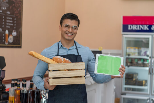  man, a small business owner, a bakery holding a tablet, smiling, happy and confident in a coffee shop and bakery. 