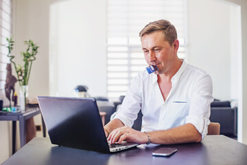Fototapeta premium Happy user holding credit card in his mouth while typing on laptop