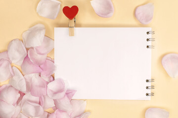 An open empty notebook with a clothespin in the shape of a heart among pink rose petals. Festive background. Space for text