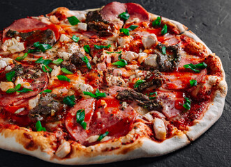 Pizza with Mozzarella cheese, salami, chicken meat, beef, ham, Tomato sauce, pepper, spices. Italian pizza on Dark grey black slate background