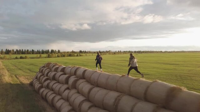 Two parkourers are running on haystacks stacked in ole at a high altitude. Shooting with a copter in motion