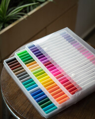 60 pieces of colorful markers in transparent plastic packaging on a wooden background.