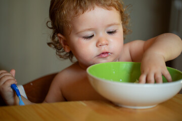 Kid baby eat soup in the kitchen with dishes and spoon.