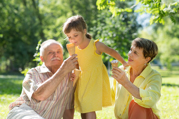 grandparents and happy child granddaughter eat ice cream in a summer park. Summer holiday
