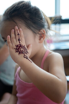 Portrait of Henna ornaments on little girl's hand covering face.