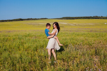 mother holds her son in her arms in the field in nature
