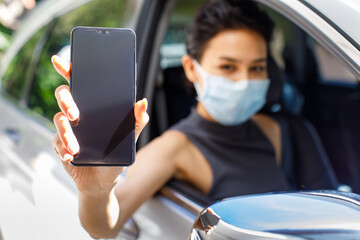 Closeup shot of blank screen mobile phone for application appointment registration copy space in female hand wearing face mask sitting in car in drive through line for coronavirus vaccination