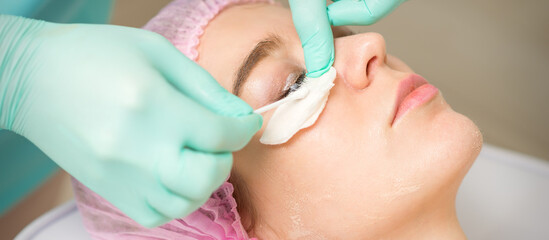 Naklejka premium Young woman receiving eyelash removal procedure and removes mascara with a cotton swab and stick in a beauty salon