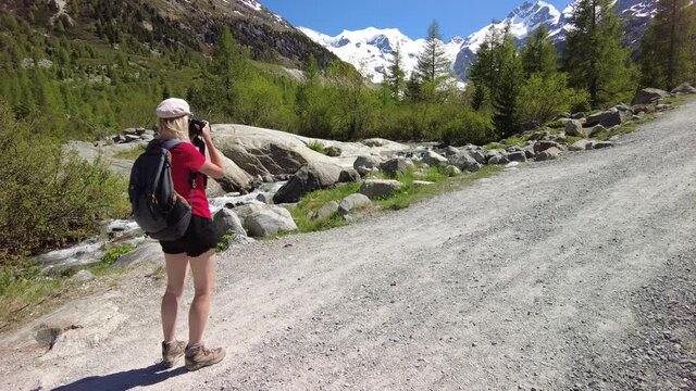 Photographer woman with a camera photographing the Morteratsch glacier on the trail in Switzerland. The biggest glacier in Bernina Range of Bundner Alps in Graubunden of Switzerland.