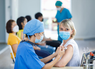 Female professional doctor wears face mask and blue hospital uniform injecting coronovirus vaccine...