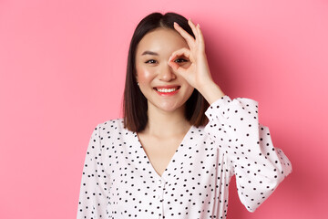 Beauty and lifestyle concept. Close-up of cute smiling asian girl showing okay sign on eye,...