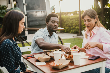 Multiracial people having fun eating at food truck outdoor - Main focus on left mature woman hand