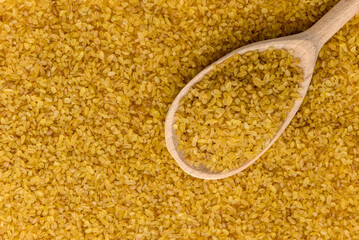 Bulgur in wooden spoon isolated on white background.