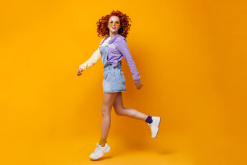Fototapeta na wymiar Lady in denim skirt and lilac sweatshirt jumps on orange background
