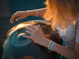 Hang close-up. Hands and hair of a girl playing the hang. Sunset.