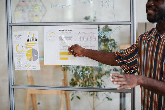African young businessman pointing at financial document on the glass wall and presenting it to his colleagues at office